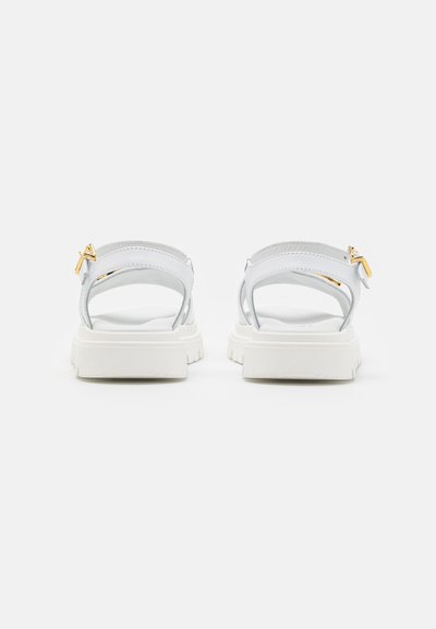 Sandali bianchi con design a due cinturini, caratterizzati da un materiale liscio, una suola spessa bianca e un dettaglio in oro su uno dei cinturini.