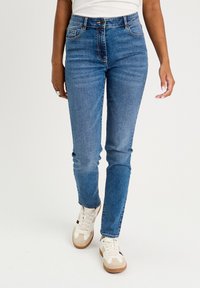 Niebieskie dżinsy o slim fit, pięciokieszeniowym designie, średnim stanie i wyblakłej teksturze, w połączeniu z białymi i beżowymi trampkami.