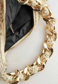 Gewebte, hellbeige Handtasche mit glänzendem, goldfarbenem Metallkettengriff, mit schwarzem Stoffinnenfutter und Reißverschlussverschluss.
