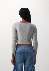 Grå, ribbet, langermet crop top med rund hals og tettsittende design. Kombinert med blå høyt midje cargo jeans med baklommer.