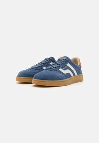 Blaue Wildledersneaker mit weißen Seitenstreifen, runder Zehenpartie und Gummisohle. Besitzt ein beiges Innenfutter und einen orangen Akzent an der Ferse.