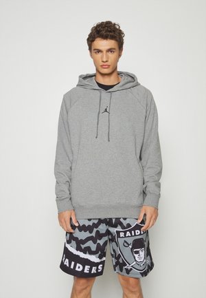Grijze capuchontrui met een zwart logo; gecombineerd met zwart-grijze camouflage shorts met een Raiders-logo. Casual sportkleding.