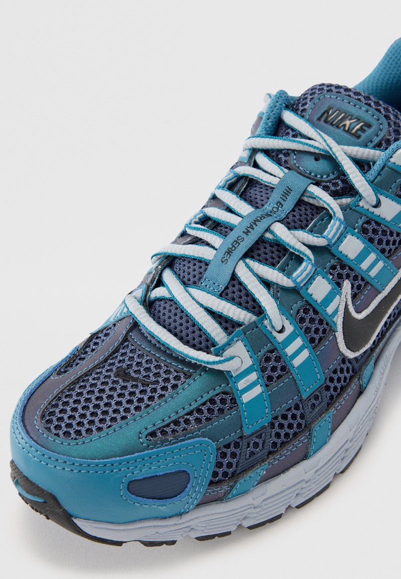 Blaue und graue Sportschuhe mit einem Mesh-Obermaterial, strukturierten Akzenten und kontrastierenden Schnürsenkeln. Enthält ein auffälliges schwarzes Logo an der Seite.