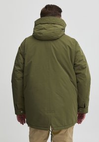 Alyvų žalia parka striukė su virvele apatinėje dalyje ir didele, siuvinėta kapuce. Savybės - mygtukais užsegamos rankovės bei lygi, matinė tekstūra.