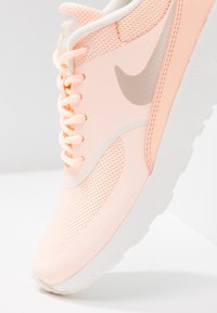 Ljust rosa Nike-sneaker som visar nätmaterial, snören och swoosh-logotyp på vit sula mot vit bakgrund.