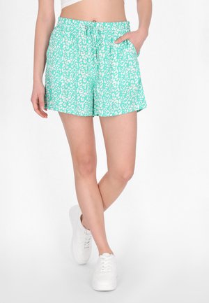 Pantaloni scurți de culoare turcoaz deschis, cu un model de frunze albe, confecționați dintr-o țesătură ușoară, dotati cu un brâu elastic și buzunare laterale. Stilizați cu adidași albi.