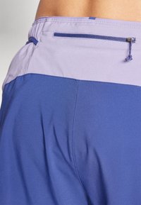 Calções roxos com uma textura suave, um cós em contraste e um bolso com zipper na parte de trás para armazenamento seguro.