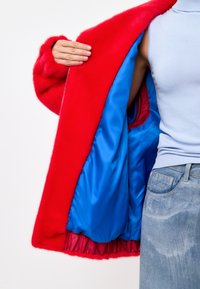 Jachetă din blană roșie cu un căptușeală din satin albastru lucios, dotată cu închidere cu fermoar și o textură moale. Interiorul include o margine roșie.