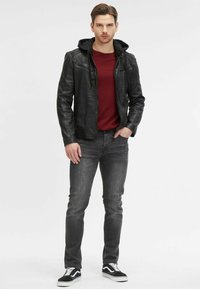 Zwarte leren jas met een hoodie, rood shirt, grijze jeans en zwarte sneakers. De jas heeft ritszakken en gestructureerde schouders.
