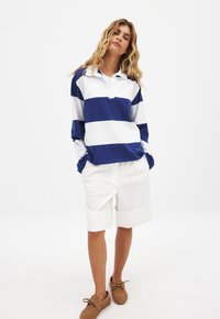 Blue and white striped long-sleeve polo shirt with a collar, paired with white folding shorts and brown lace-up shoes.