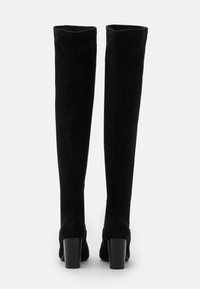 Botas negras de ante por encima de la rodilla, con una textura suave, tacón ancho y borde superior redondeado. Diseño simple sin embellecimientos adicionales.