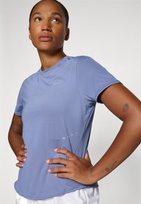 T-shirt de sport à manches courtes en tissu bleu clair. Il présente un col rond, un logo Nike et de subtils accents réfléchissants sur le côté.