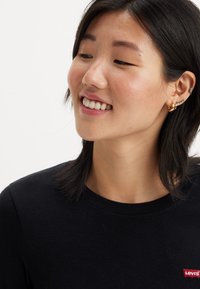 Chemise noire à manches longues avec un col arrondi, dotée d'un petit patch logo Levi’s rouge sur le côté gauche de la poitrine. Tissu lisse et léger.