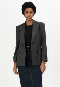 Blazer gris à rayures, double boutonnage, avec des revers en pointe, des épaulettes et deux poches avant, associé à un haut noir et une jupe en denim.