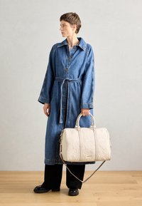 Trench en jean avec une ceinture, présentant de grands boutons et des poches latérales ; sac à main blanc matelassé avec double poignée et bandoulière amovible.