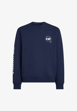 Tumesinise puuvillaseguga dressipluus, millel on rinnal väike tikandiga päikeseprillide graafika ja vasakul varrukal tekst.