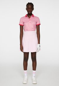 Rosa mönstrad polo tröja med korta ärmar, tillsammans med en plisserad ljusrosa kjol. Vit handske på vänster hand, vita skor och rosa strumpor.