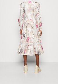 Robes midi à imprimé floral en tissu transparent, avec des manches bouffantes, un ourlet volants et des détails de finition contrastés dans des tons rose pastel et crème.