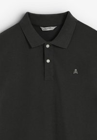 Camisa polo negra hecha de tela texturizada. Cuenta con un cuello, una tapeta de botones y un pequeño logotipo de calavera en gris en el lado izquierdo del pecho.