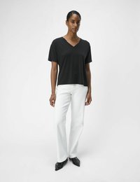Sort kortærmet V-hals top med løs pasform, parret med hvide vidde jeans og sorte spidse sko. Enkel og moderne design.