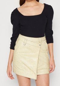 Schwarzer, gerippter Langarm-Top mit quadratischem Ausschnitt; goldfarbener, strukturierter Minirock mit Wickeldesign und seitlicher Nahtdetail.