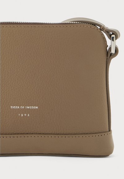 Borsa in pelle marrone con finitura testurizzata, chiusura con zip e accessori in argento. Presenta il logo impresso "TIGER OF SWEDEN 1903."