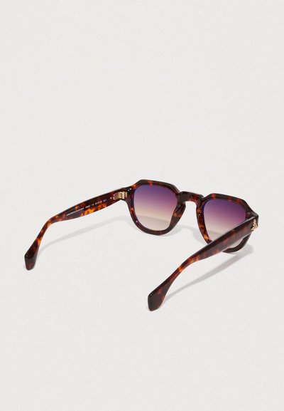Gafas de sol de carey con montura hexagonal, lentes púrpuras degradados y detalles dorados en las patillas. Acabado suave.