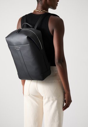 Black leather backpack with a structured design, featuring a top handle, adjustable straps, and a zippered closure. Notable logo detail.