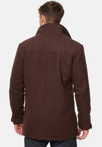 Bruine wolmix jas met hoge kraag, rugpas en lange mouwen. Heeft een rechte snit en minimale details op de achterkant.