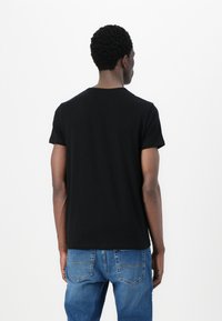 T-shirt nera a maniche corte in cotone, con scollo rotondo e vestibilità rilassata. Indossata con jeans in denim blu.