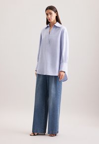 Camicia a righe blu chiaro con colletto, mezzo bottone e maniche ampie abbinata a pantaloni in denim blu a vita alta e gamba larga.