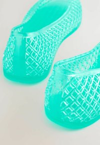 Permatomi melsvai žali plastikiniai šlepetės su tekstūruotu deimantiniu raštu. Suapvalinti pirštai ir žemi kulniukai, tinkami kasdieniam dėvėjimui.