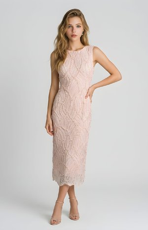 Mujer con cabello rubio largo que lleva un vestido midi texturizado sin mangas de color rosa pálido y tacones de tiras color nude, de pie frente a un fondo gris liso.