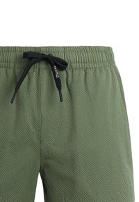 Groene korte broek van gestructureerde stof met elastische tailleband en zwart trekkoord, met een klein wit "Protest" logo.