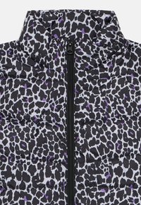 Veste noire et blanche en imprimé léopard matelassée avec des accents violets, dotée d'un col haut et d'une fermeture éclair à l'avant. Tissu texturé avec un design matelassé.