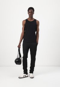 Musta ribbed toppi, mustat slim-fit housut, valkoiset lenkkarit, joissa on harmaita ja mustia yksityiskohtia, ja pieni musta laukku kädessä. Minimalistinen muotoilu, neutraalit värit.
