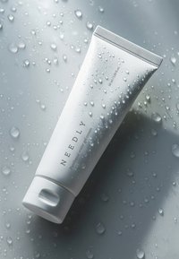Tube blanc de crème gel aqueuse "NEEDLY" à la panthénol avec un bouchon texturé, présentant des gouttes d'eau sur un fond gris. Taille indiquée : 50 ml.