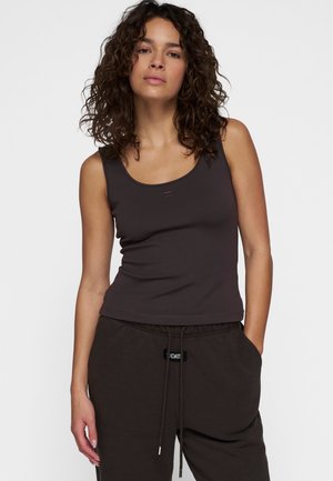 Donkerbruine tanktop van stretchy stof, met een ronde halslijn en smalle schouderbandjes, gecombineerd met loszittende donkere joggingbroeken.