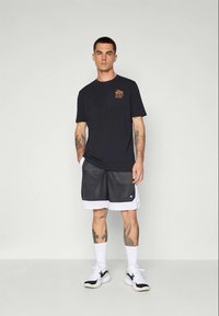 Marineblå t-shirt med orange brystgrafik, parret med sorte mesh shorts med hvidt trim, og hvide sneakers med sorte accenter.