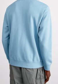 Ljusblå sweatshirt i mjukt material med långa ärmar och en klassisk rund halsringning. Nederkant och ärmslut är ribbade, med sömlös baksidesdesign.