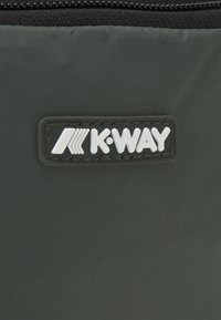 Polo značky K-Way v tmavosivej tkanine, s výraznou bielou nášivkou loga a textúrovaným povrchom so vzorom mriežky.