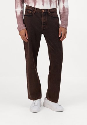 Brune denimjeans med rett snitt, med fem lommer, synlig søm og slitt utseende, kombinert med hvite sneakers.