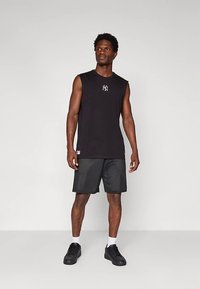 Black sleeveless shirt with white NY logo, paired with black mesh shorts and black sneakers. Features a relaxed fit and soft fabric.