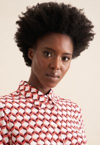 Camicia button-up con un motivo ondulato rosso, bianco e bordeaux, dotata di colletto classico e una texture di tessuto morbida.