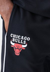 Crne trenirke s crvenim logotipom Chicago Bullsa. Logotip uključuje glavu bika s bijelim rogovima i podebljanim tekstom u bijeloj boji iznad.