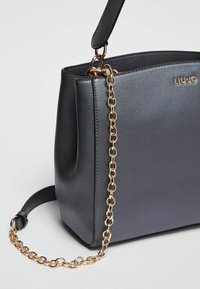 Sac à main noir texturé avec une bandoulière en chaîne dorée et un détail de logo. Présente une forme structurée et deux options de port.