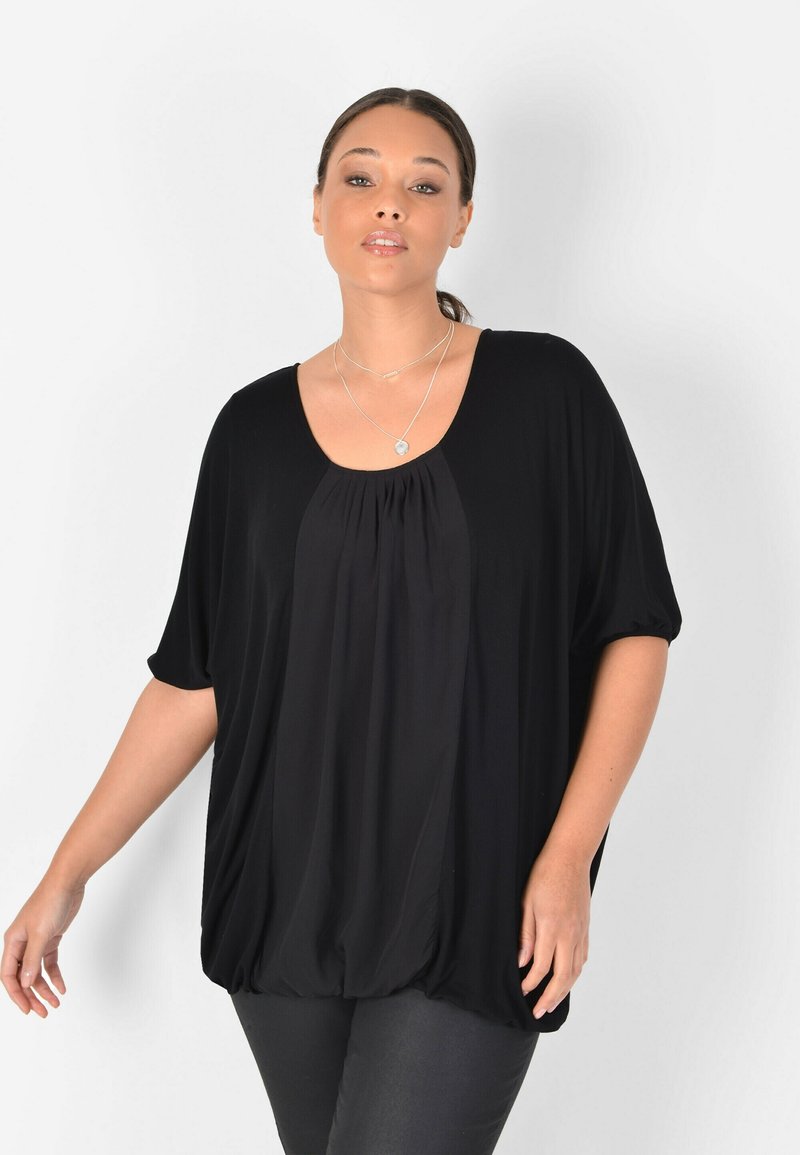 Top negro de corte holgado con mangas cortas, escote redondeado y tela fruncida en el pecho. Textura suave, adecuada para un uso casual.