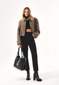 Rudos spalvos trumpa striukė, juodas golfas, juodos siūtos kelnės, juodi patentinės odos batai su stambiais kulnais ir tekstūruota juoda rankinė-tote.