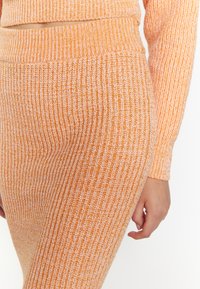 Orange Rippstrickrock mit strukturierter Oberfläche und elastischem Bund, der durch kontrastierende hellere Fäden ergänzt wird. Nahaufnahme.