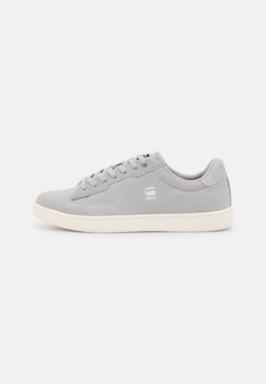 Gray canvas sneakers with a low profile, round toe, and white rubber sole; features lace-up design and branding on the side.